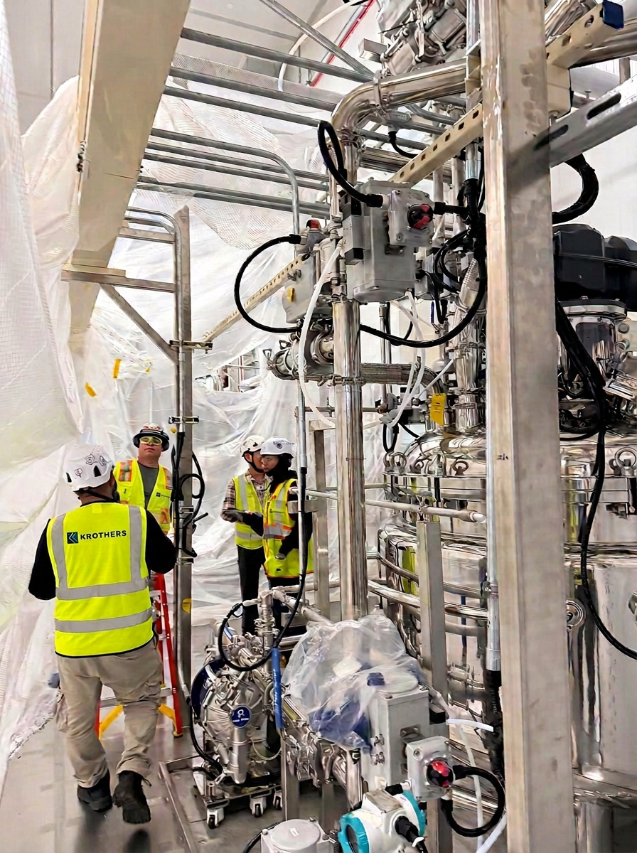 KROTHERS field personnel inspect installed process equipment inside an active industrial work area.