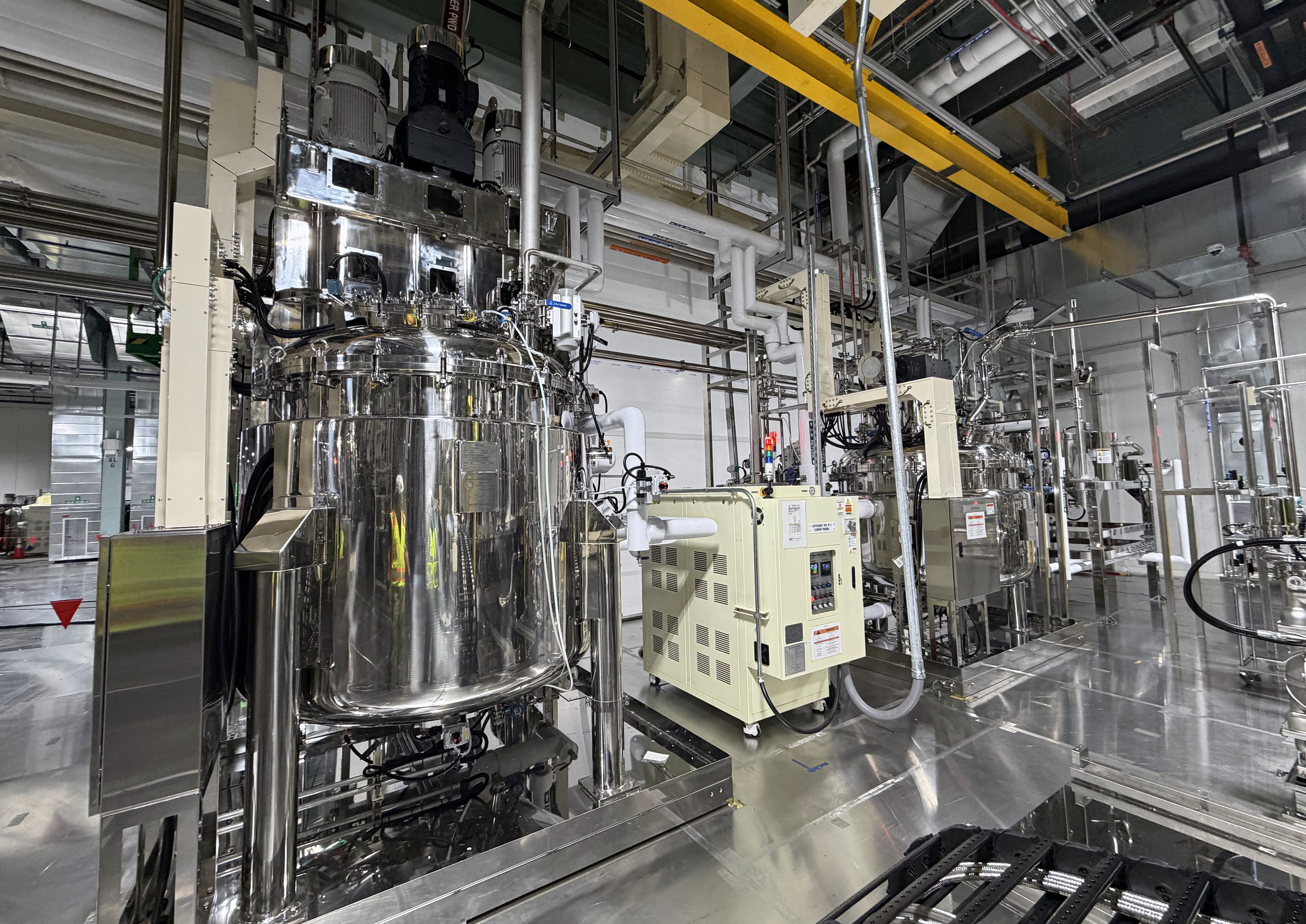 A large stainless process vessel with adjacent controls and utility piping inside an industrial facility.