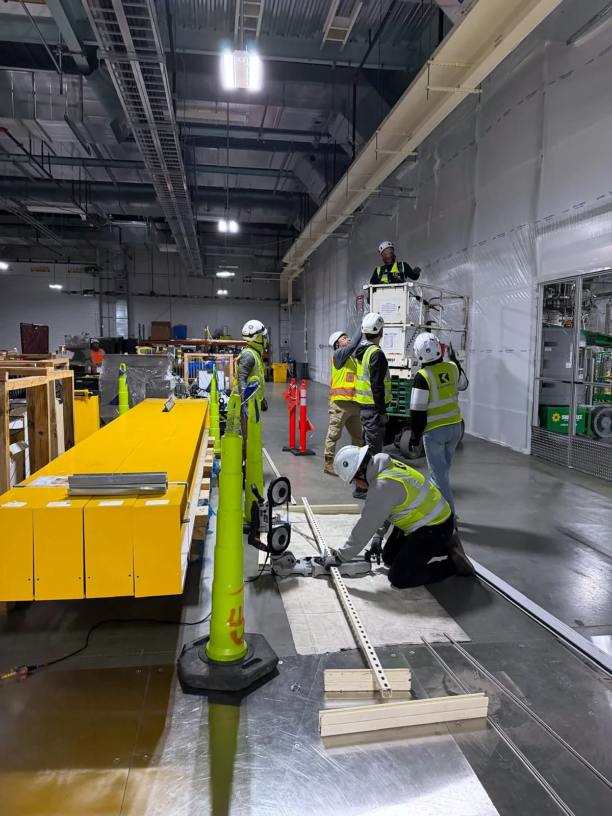 Field crew cutting and positioning strut while elevated work continues inside an industrial facility.